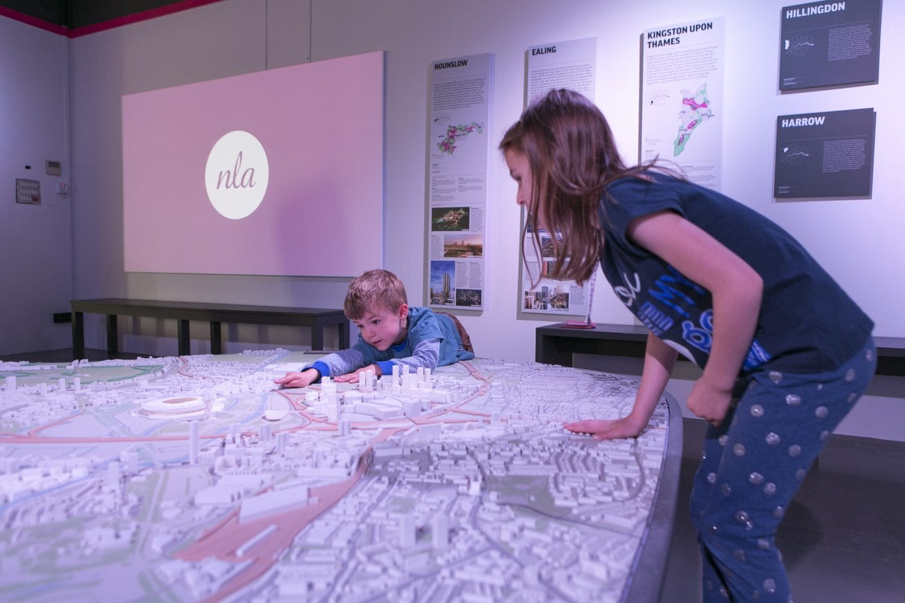 A child is engaged in an activity along with it's mother, pointing to a building on a map.