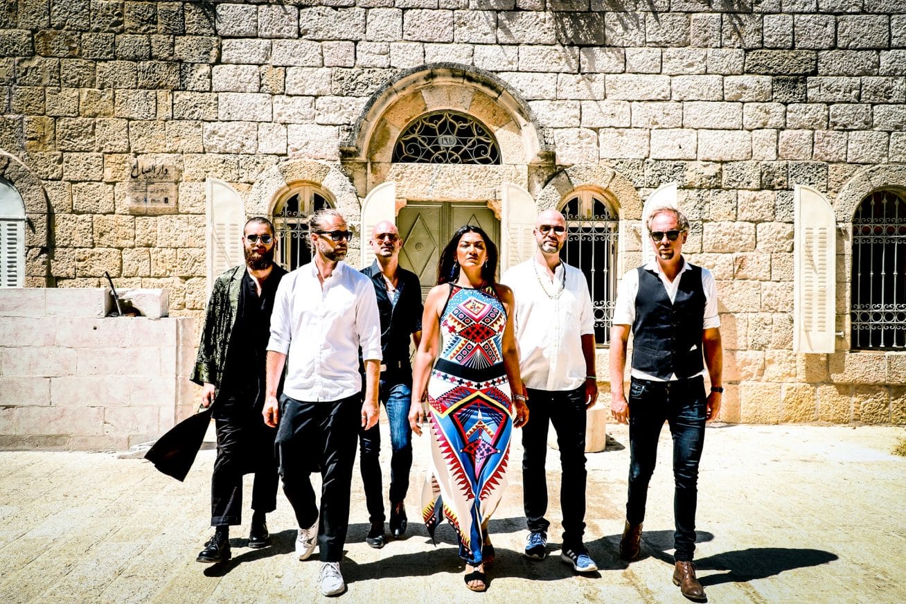 6 band members pose in a line in front of a house