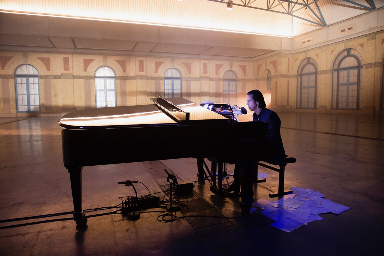 Nick Cave sat at a black grand piano within the beautifully up-lit Alexandra Palace